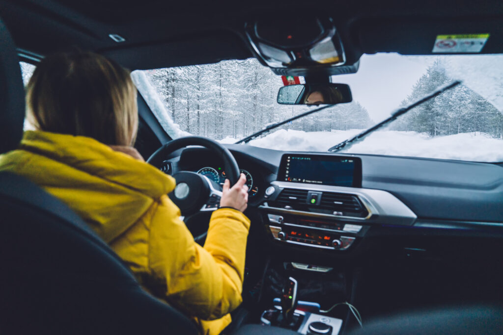 Cropped image of woman holding hands on helm driving on snowy off road in wood during expedition